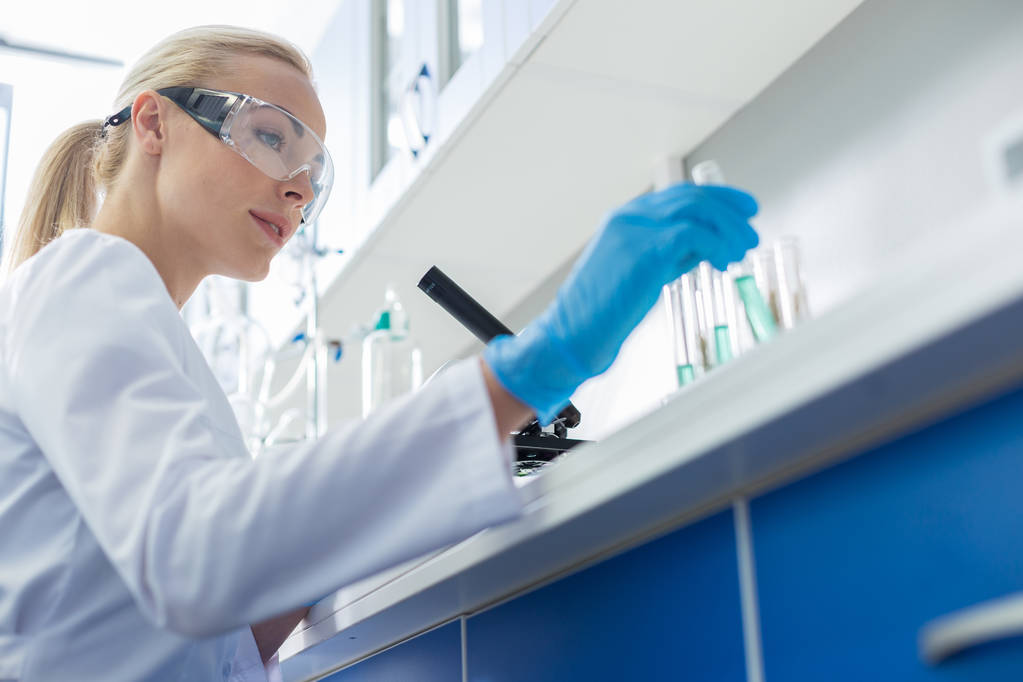 Modernia tiedettä. Positiivinen älykäs naispuolinen tutkija hymyilee ja rei 'ittää koeputkea työskennellessään kemiallisessa laboratoriossa
 - Valokuva, kuva