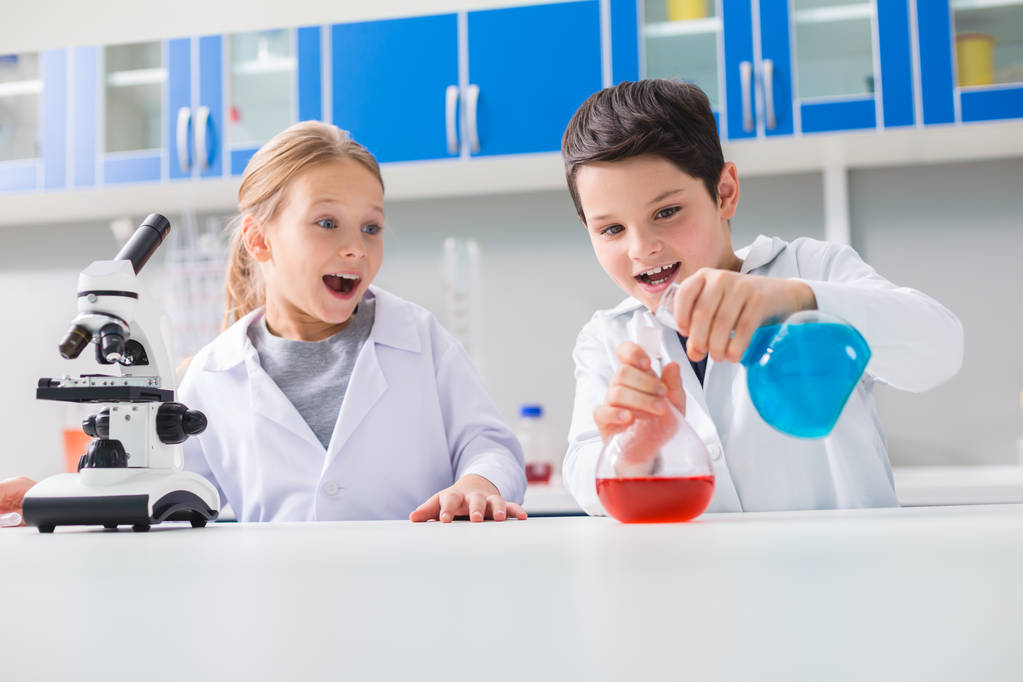 Interessante Chemie. positiver freudiger intelligenter Junge, der im Labor Flaschen hält und chemische Reagenzien mischt - Foto, Bild