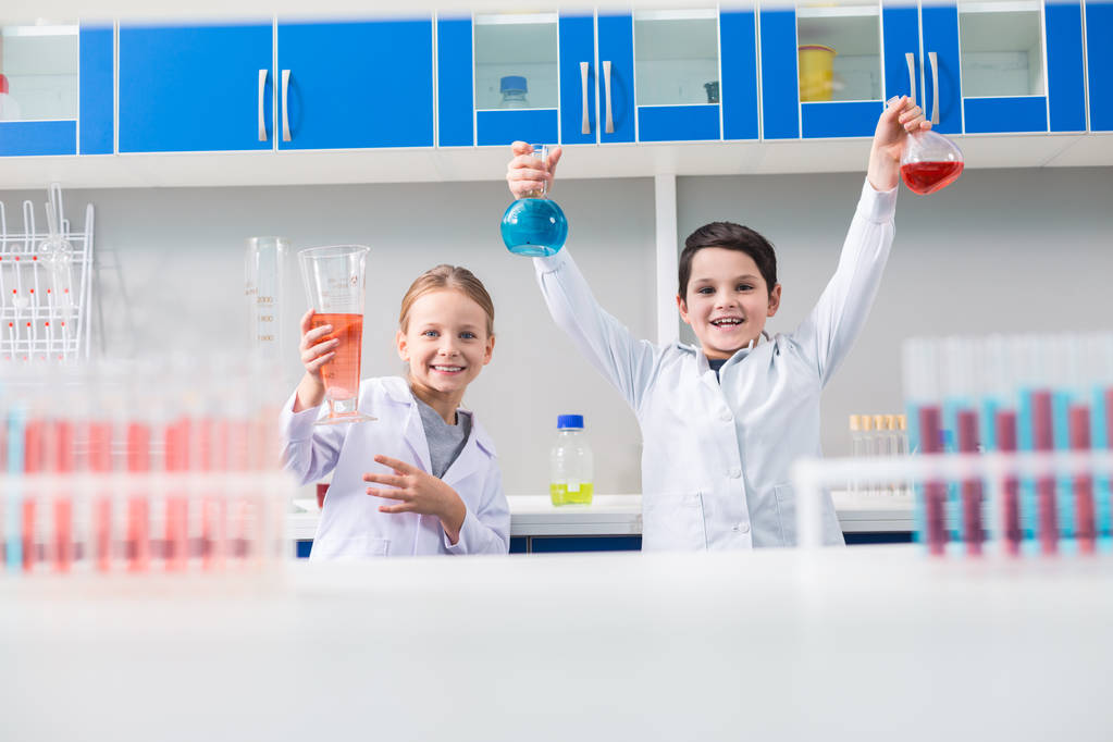 ラボで化学研究室にいる間、笑顔であなたを見ているポジティブな喜びの幼い子供たち - 写真・画像