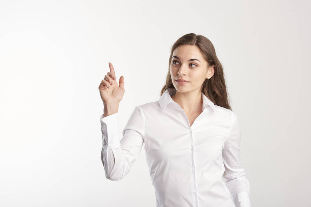 Retrato de jovem mulher vestindo camisa branca e olhando para cima, apontando para o espaço de cópia com o dedo. Fundo branco isolado
.  - Foto, Imagem