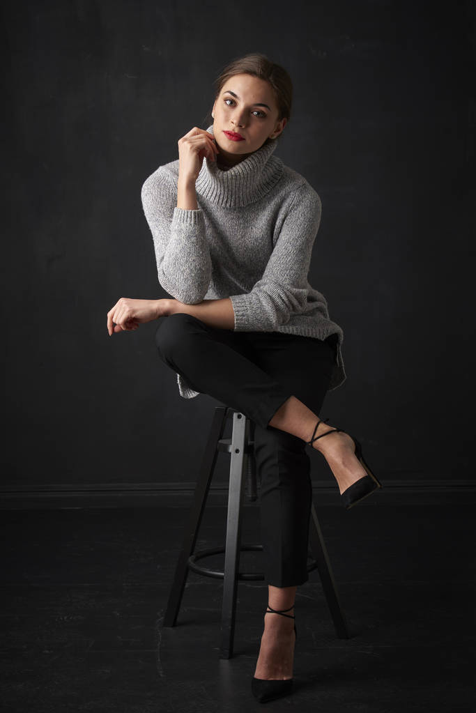 Повнометражний знімок привабливої молодої жінки в светрі з черепашками сидячи на темному тлі і розслабляючись
.  - Фото, зображення