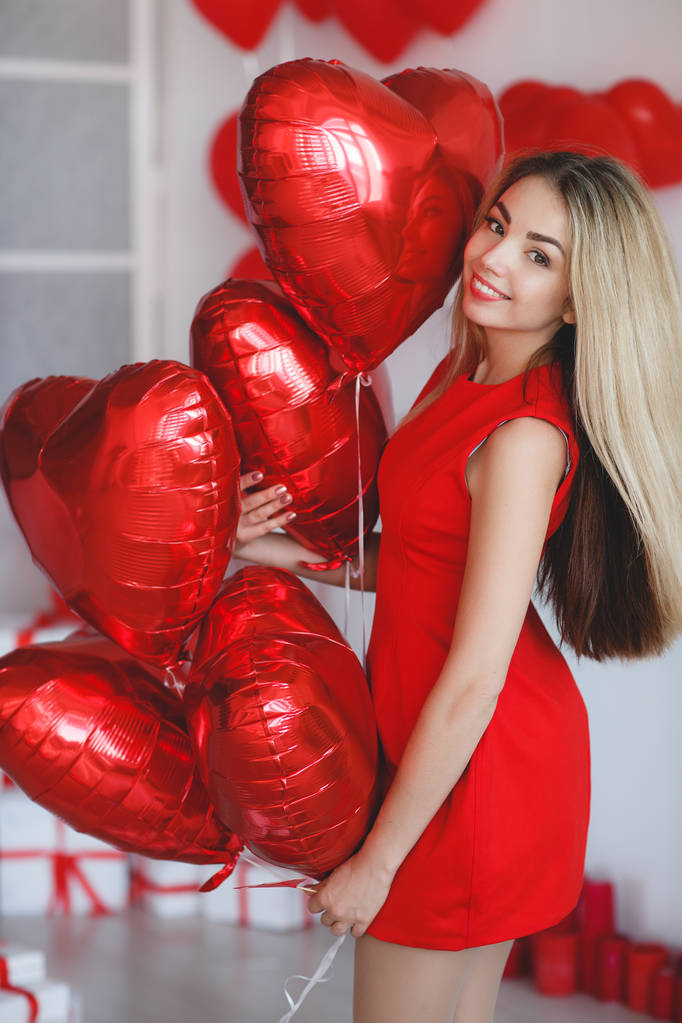 Schoonheid Valentijnsdag vrouw met rode ballonnen. Fashion Model meisje gezicht profiel portret met rode ballonnen in de vorm van hart in haar hand. Rode lippen en nagels. Roze onscherpe achtergrond. Mooie luxe make-up en Manicure, haren. - Foto, afbeelding