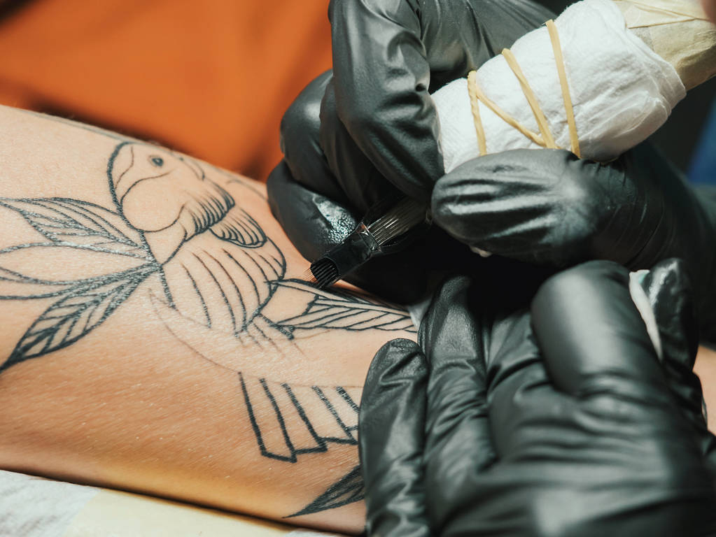 Artista de tatuagem no trabalho. Mulher de luva de látex preto tatuando um jovem homem mão com imagem colorida em estúdio. Macro
. - Foto, Imagem