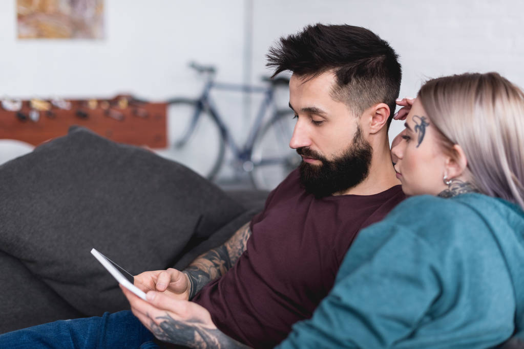 pareja tatuada mirando la tableta en el sofá en casa
 - Foto, imagen