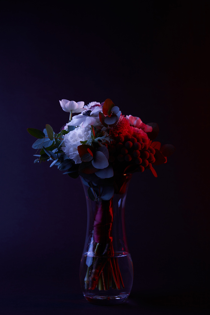 bouquet of different flowers in glass vase with red light on dark - Photo, Image