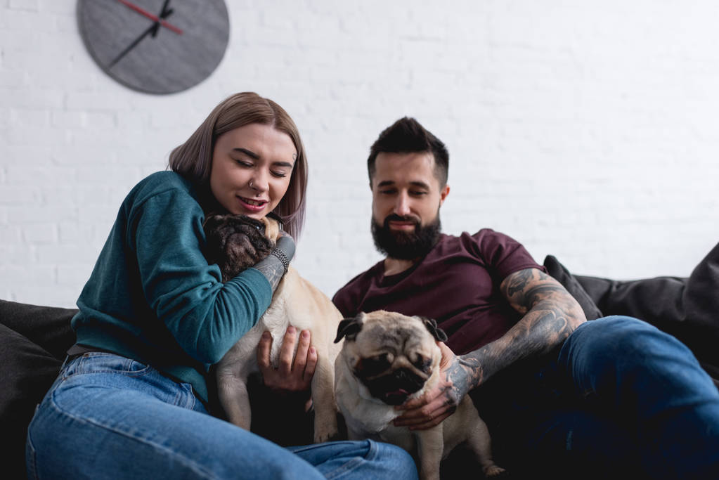 tattooed girlfriend hugging pug dog on sofa at home - Photo, Image