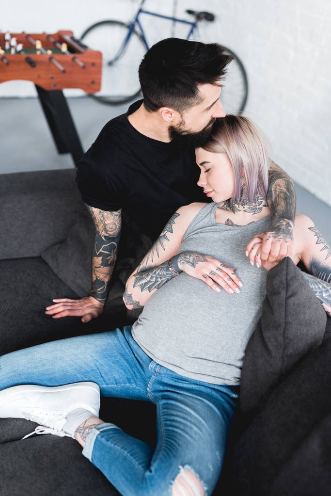 aus der Vogelperspektive: Tätowierter Freund umarmt schwangere Freundin auf dem heimischen Sofa - Foto, Bild