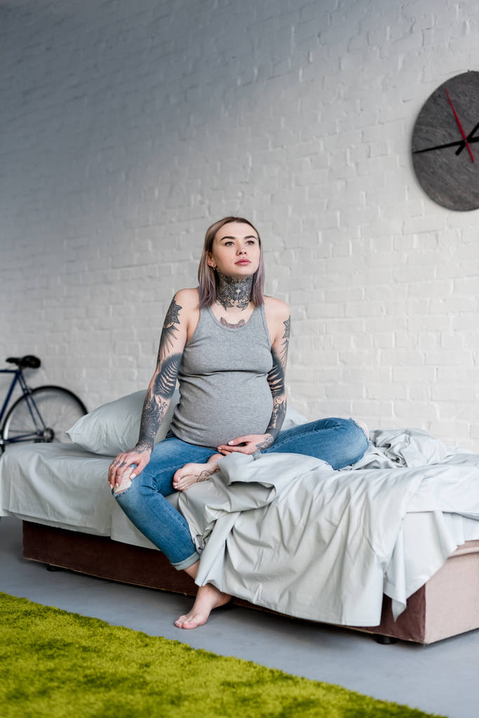 беременная женщина с татуировкой сидит дома на кровати
 - Фото, изображение