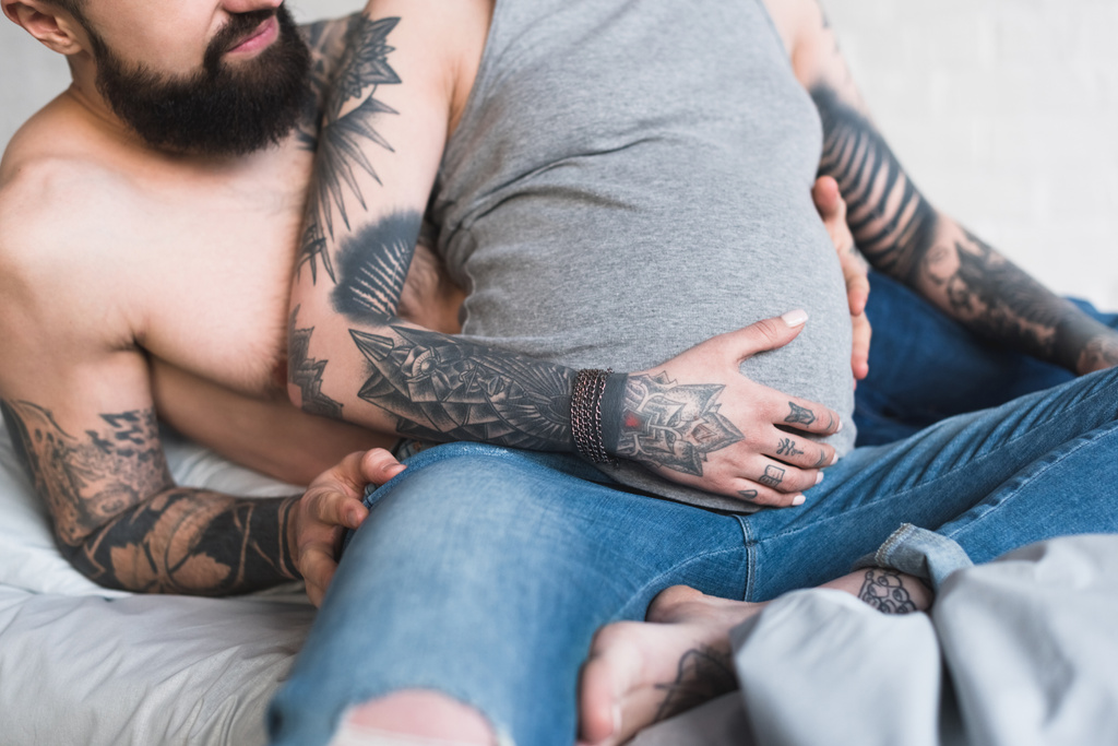 обрезанный образ парня, обнимающего беременную татуированную подружку на кровати
 - Фото, изображение