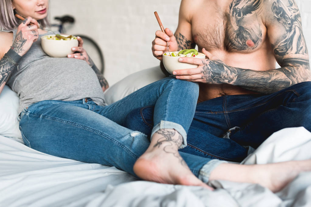 przycięty obraz w ciąży tatuażem dziewczyny jedzenie Sałatka z chłopakiem w domu - Zdjęcie, obraz