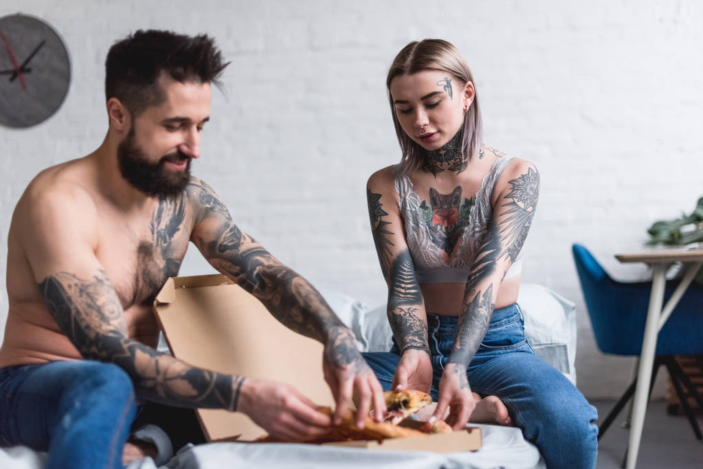Tätowiertes Paar nimmt Pizza zu Hause im Bett ein - Foto, Bild