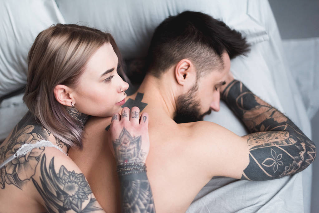 high angle view of tattooed shirtless couple lying on bed - Photo, Image