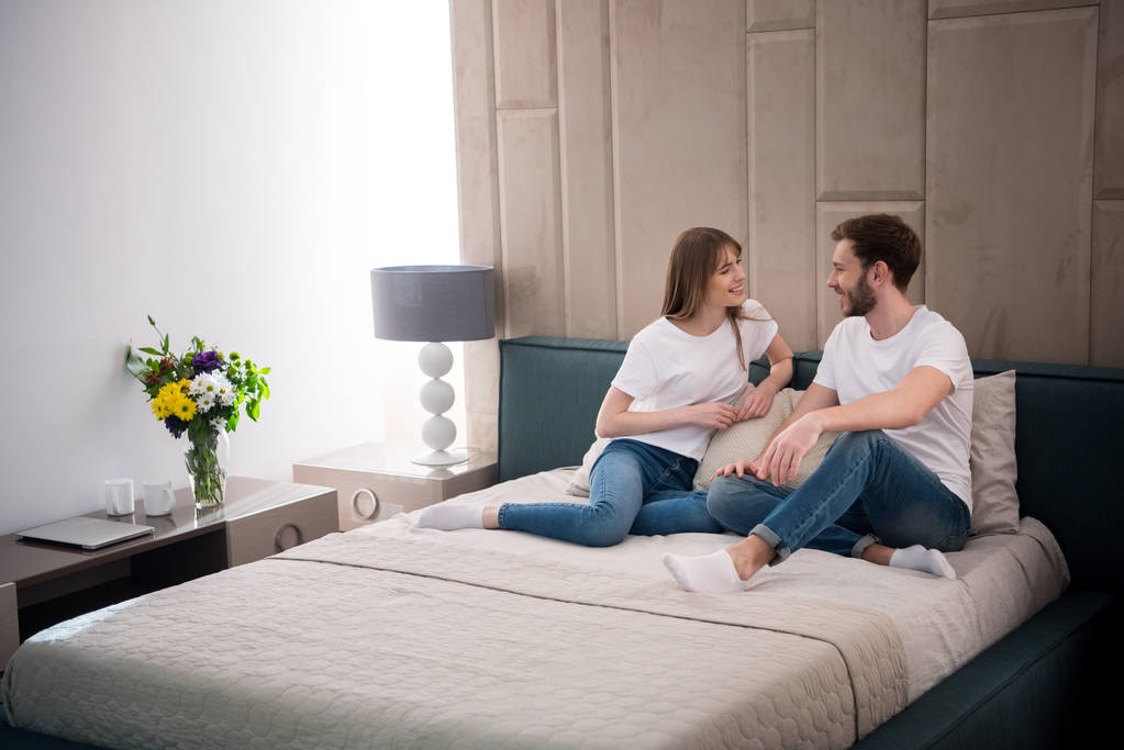 Ευτυχισμένο ζευγάρι κάθεται στο κρεβάτι σε άνετη μοντέρνα κρεβατοκάμαρα - Φωτογραφία, εικόνα