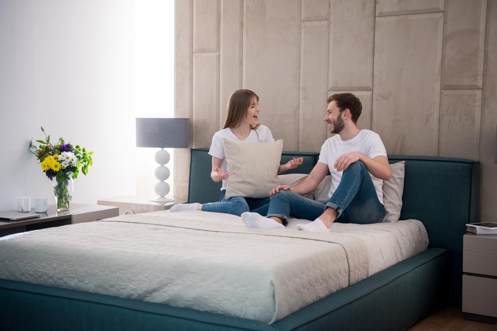 Giovane donna che tiene il cuscino e parla con il suo ragazzo in camera da letto moderna
 - Foto, immagini