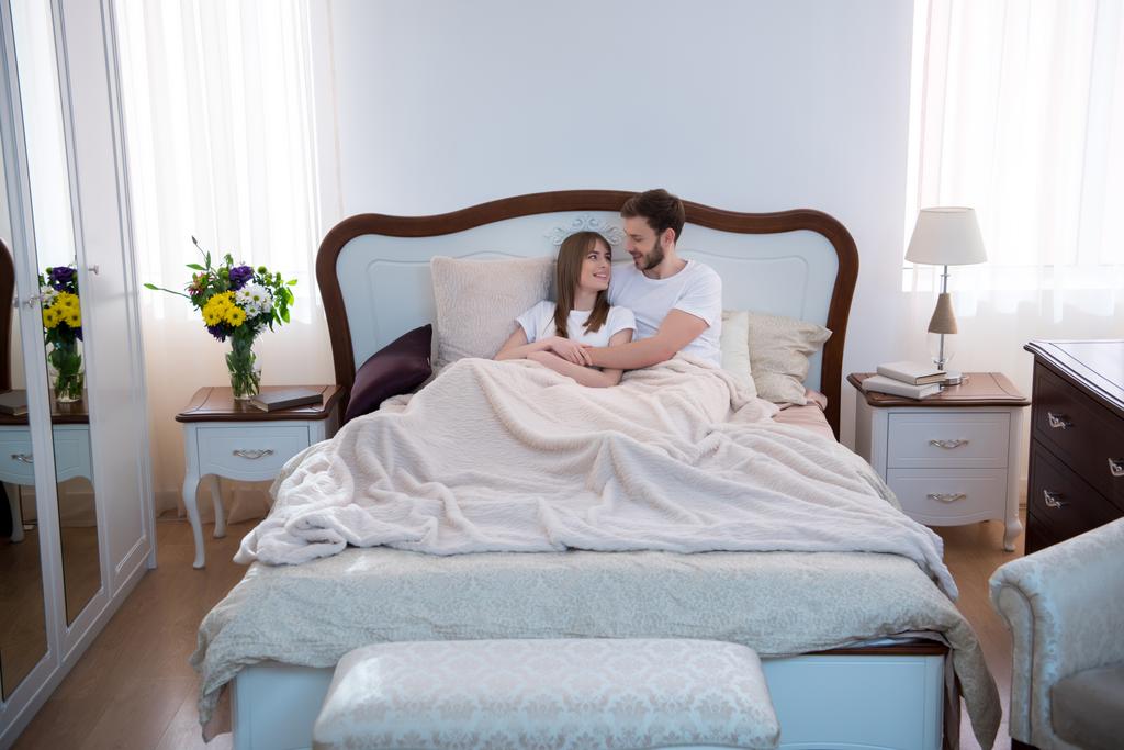 Счастливая пара обнимается в спальне с дизайнерским интерьером
 - Фото, изображение