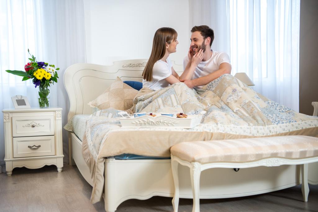 Vista lateral de la joven mujer tocando la cara del novio en el dormitorio moderno
 - Foto, imagen