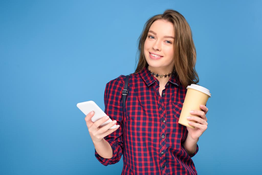 belle fille souriante avec café à l'aide d'un smartphone, isolé sur bleu
 - Photo, image