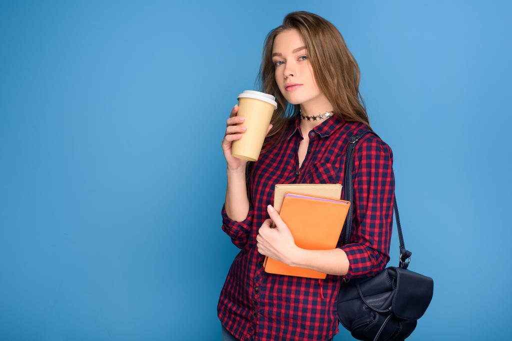 молодая студентка, стоящая с книгами и кофе на подходе, изолированная на голубом
 - Фото, изображение