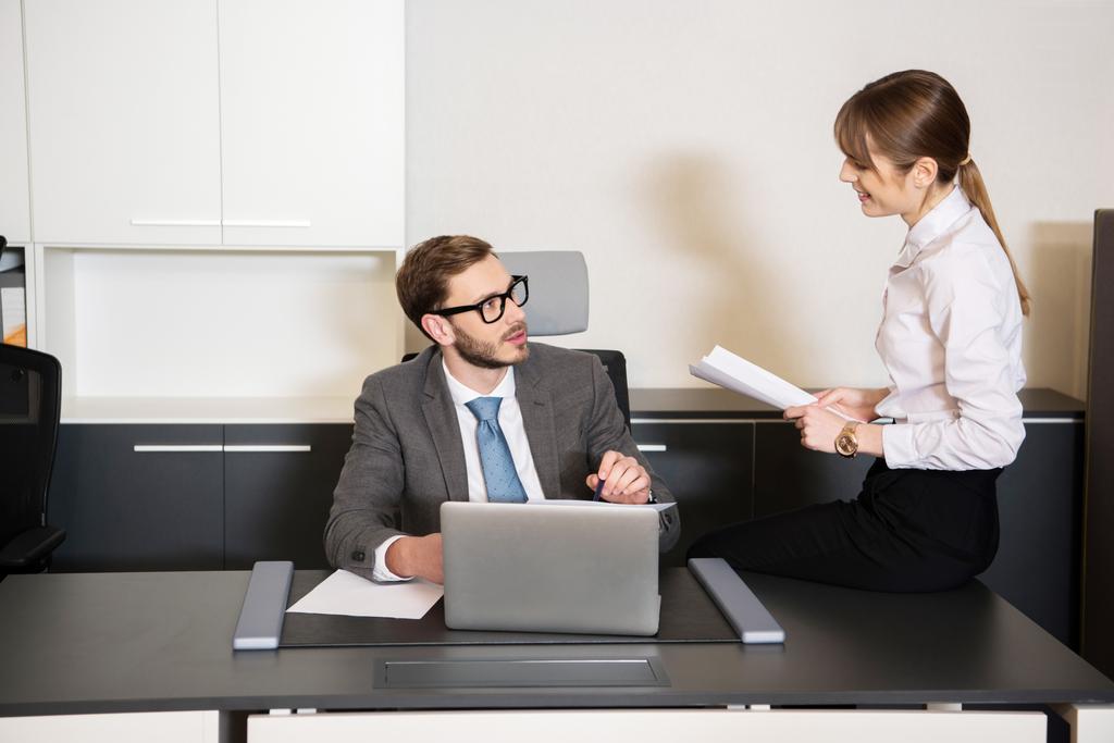 Бізнесмен за столом з ноутбуком розмовляє з колегою в офісі
 - Фото, зображення