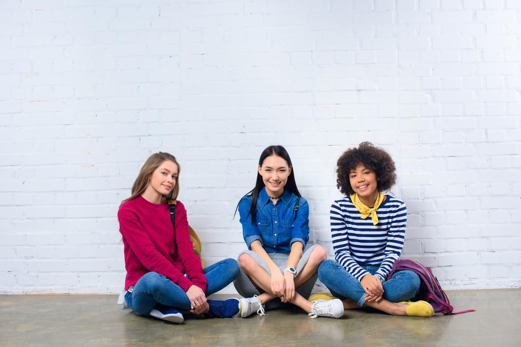 grupo de estudantes multirraciais sentados no chão contra parede de tijolo branco
 - Foto, Imagem