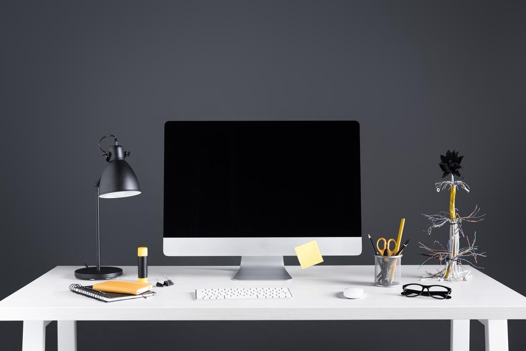 настольный компьютер с чистым экраном, лампой и офисными принадлежностями на столе на сером
 - Фото, изображение