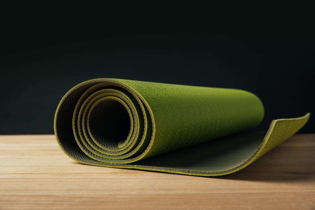 green rolled yoga mat on wooden surface on black - Photo, Image