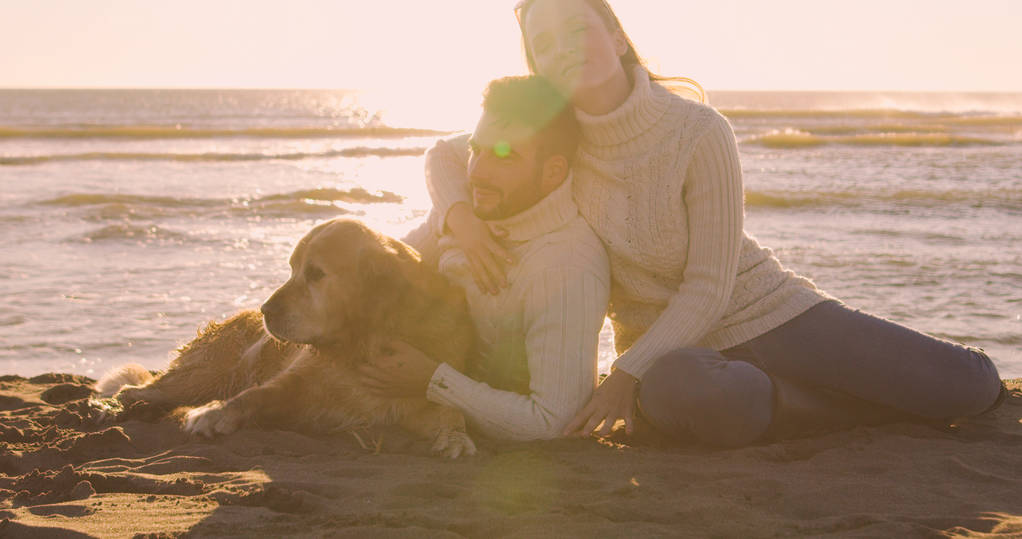 Pareja con un perro disfrutando de tiempo juntos en la playa en el día de otoño - Foto, imagen