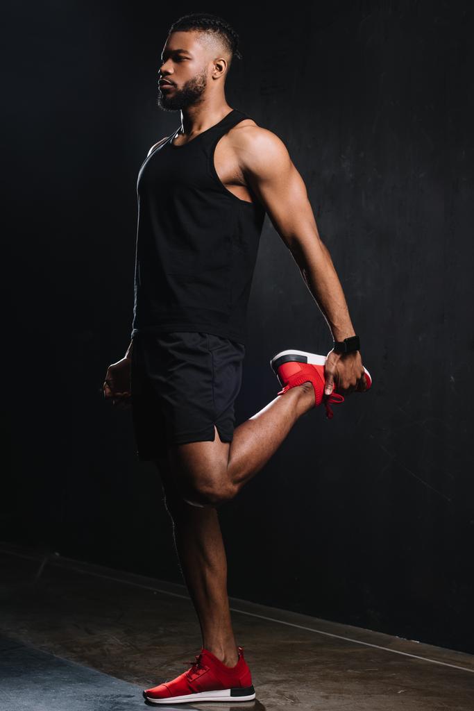 黒の上の筋肉のストレッチ若いアフリカ系アメリカ人のスポーツマンの全長ビュー  - 写真・画像