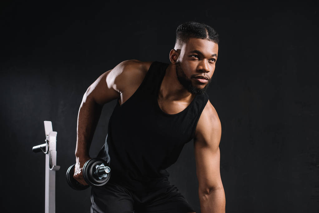 young african american sportsman exercising with dumbbell and looking away on black - Photo, Image