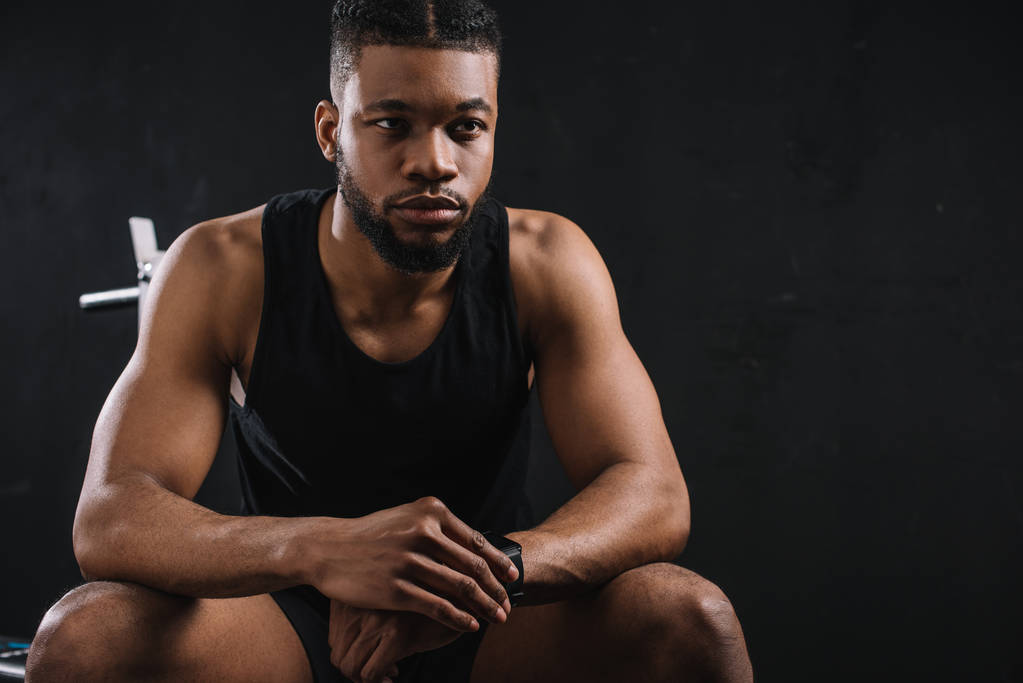 guapo joven afroamericano deportista sentado y mirando hacia otro lado en negro
 - Foto, Imagen