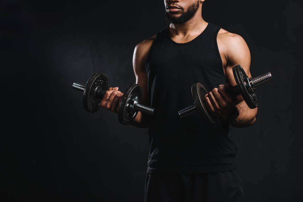 recortado shot de muscular africano americano hombre ejercitando con dumbbells aislado en negro
 - Foto, imagen