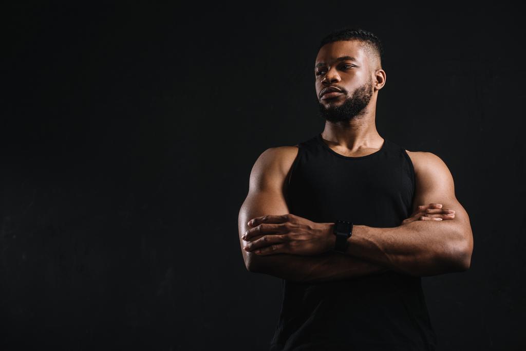 nízký úhel pohledu jistý africký americký sportovec stojící s překřížené ruce a při pohledu od izolovaných na černá - Fotografie, Obrázek
