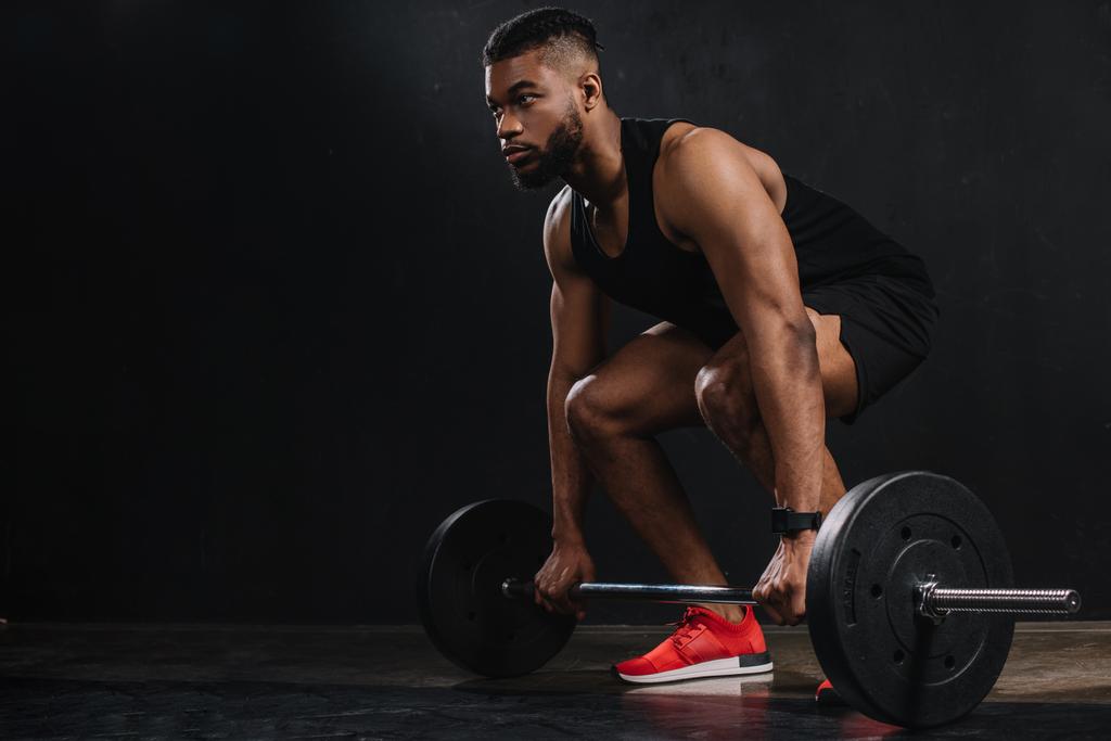 muscoloso giovane sportivo afroamericano sollevamento bilanciere e distogliendo lo sguardo sul nero
 - Foto, immagini