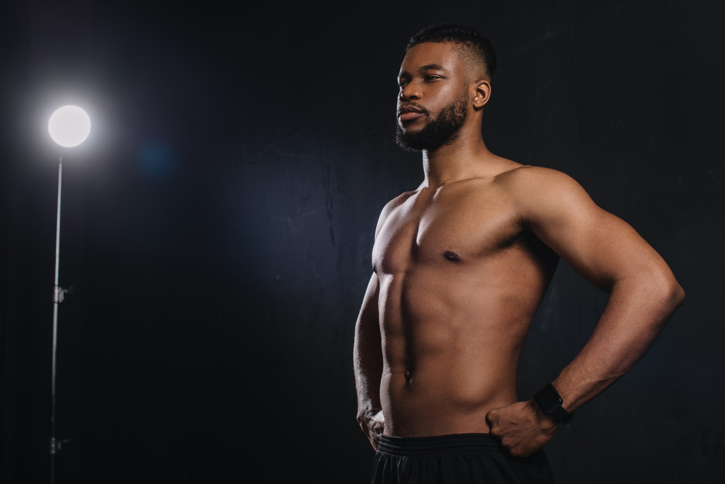 м'язистий молодий афроамериканський спортсмен, що стоїть з руками на талії і дивиться в очі на чорний
 - Фото, зображення