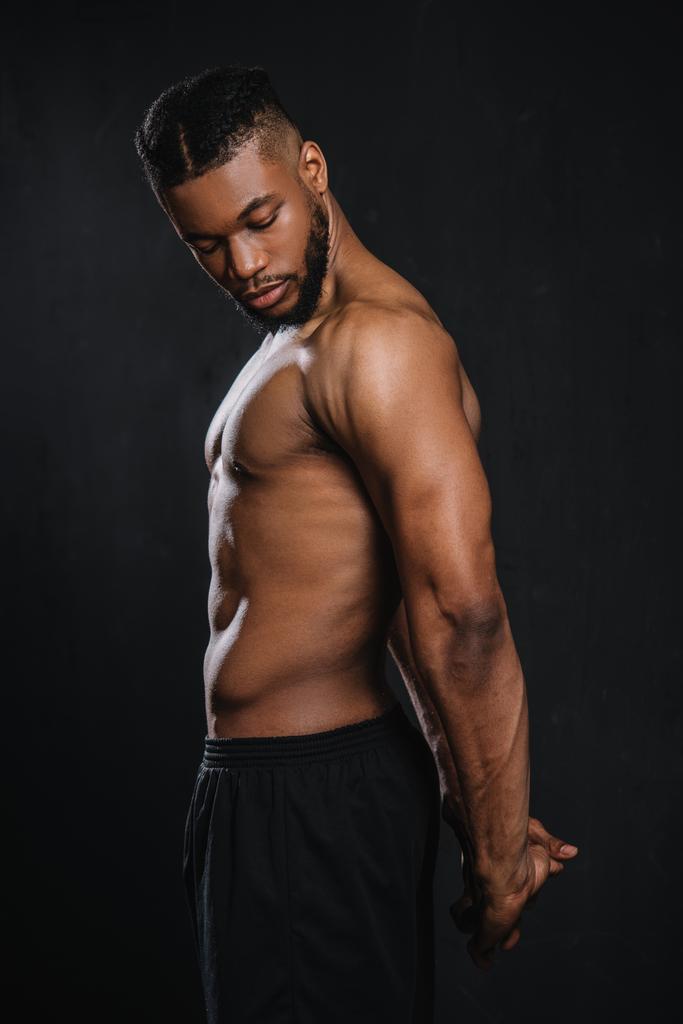 vista lateral de shirtless muscular jovem afro-americano homem esticando as mãos isoladas no preto
  - Foto, Imagem