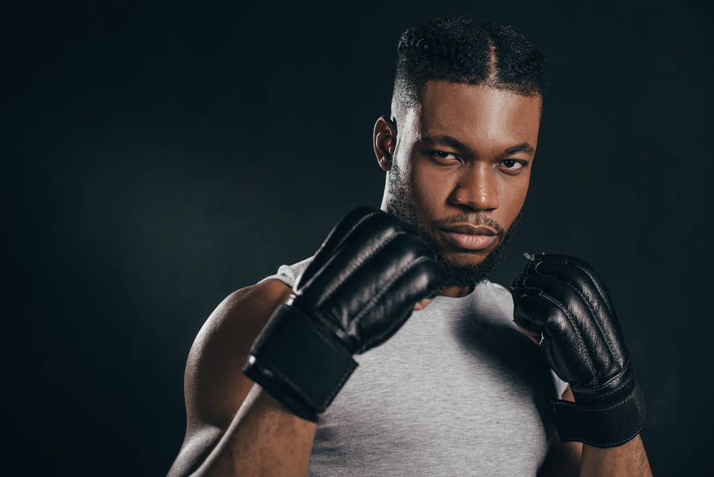 sérieux jeune afro-américain kickboxer dans gants regarder caméra isolé sur noir
  - Photo, image