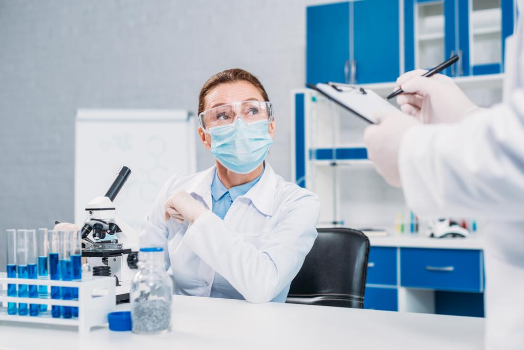 частковий погляд вчених у медичних масках та окулярах, що працюють над науковими дослідженнями в лабораторії
 - Фото, зображення