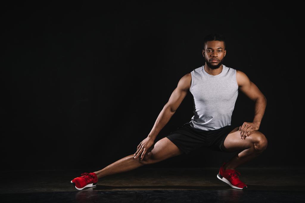 atlético joven afroamericano hombre en ropa deportiva ejercicio y mirando a la cámara en negro
 - Foto, imagen