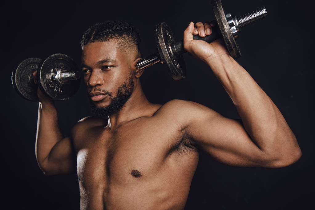 muscular sem camisa Africano americano desportista formação com halteres e olhando para longe isolado no preto
 - Foto, Imagem