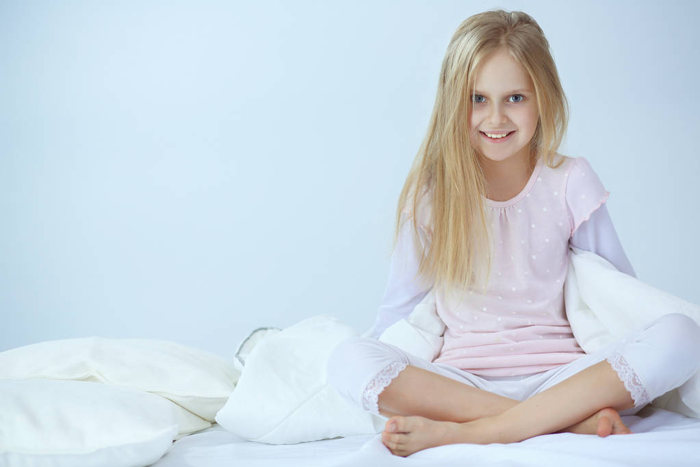 La niña en el dormitorio está sentada en la cama. La niña está usando un pijama y sentada en la cama
 - Foto, imagen