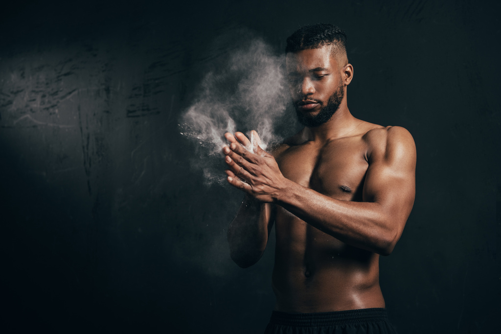 jeune sportif afro-américain à poitrine nue appliquant de la poudre de talc sur les mains sur du noir
    - Photo, image