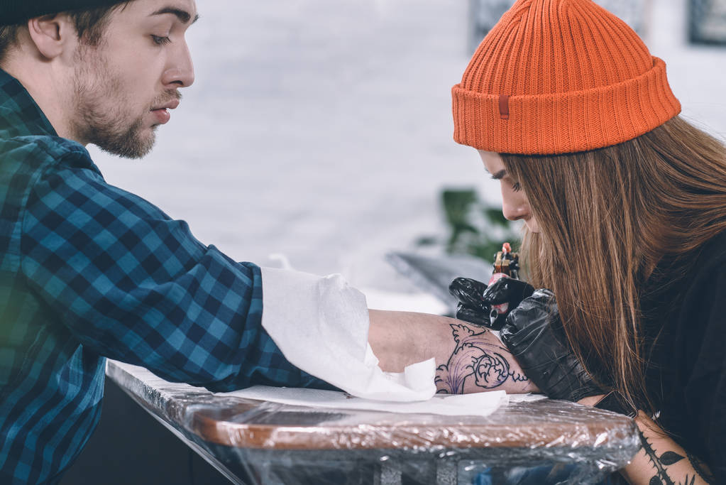 Koncentrovaná umělce v rukavice pracují na paži kus tetování ve studiu - Fotografie, Obrázek