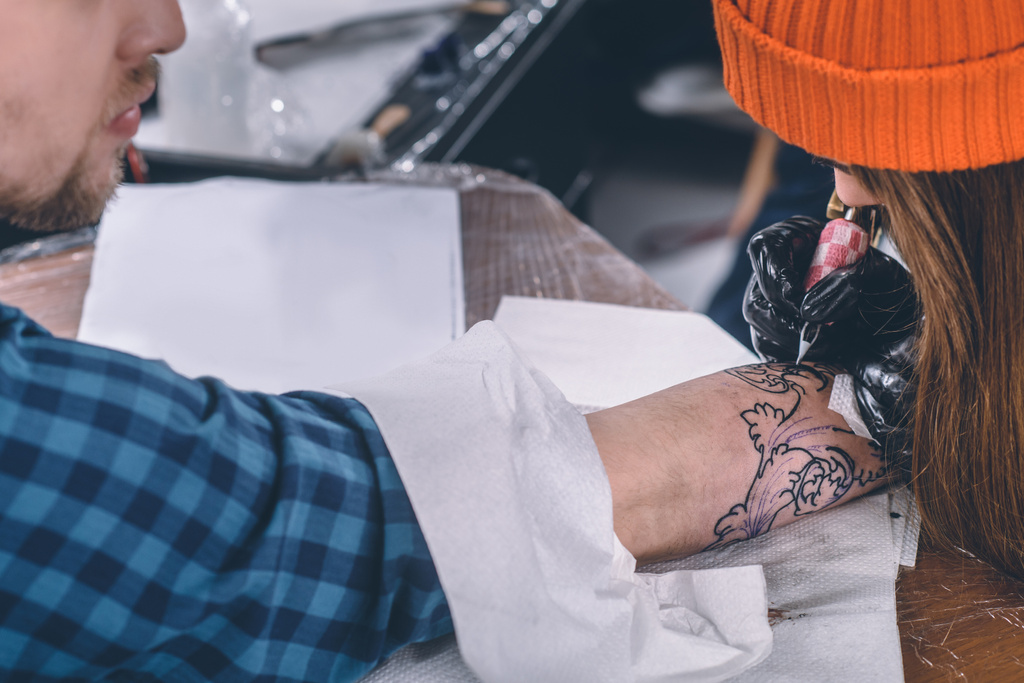 Artista del tatuaje en guantes trabajando en pieza de brazo en estudio
 - Foto, Imagen