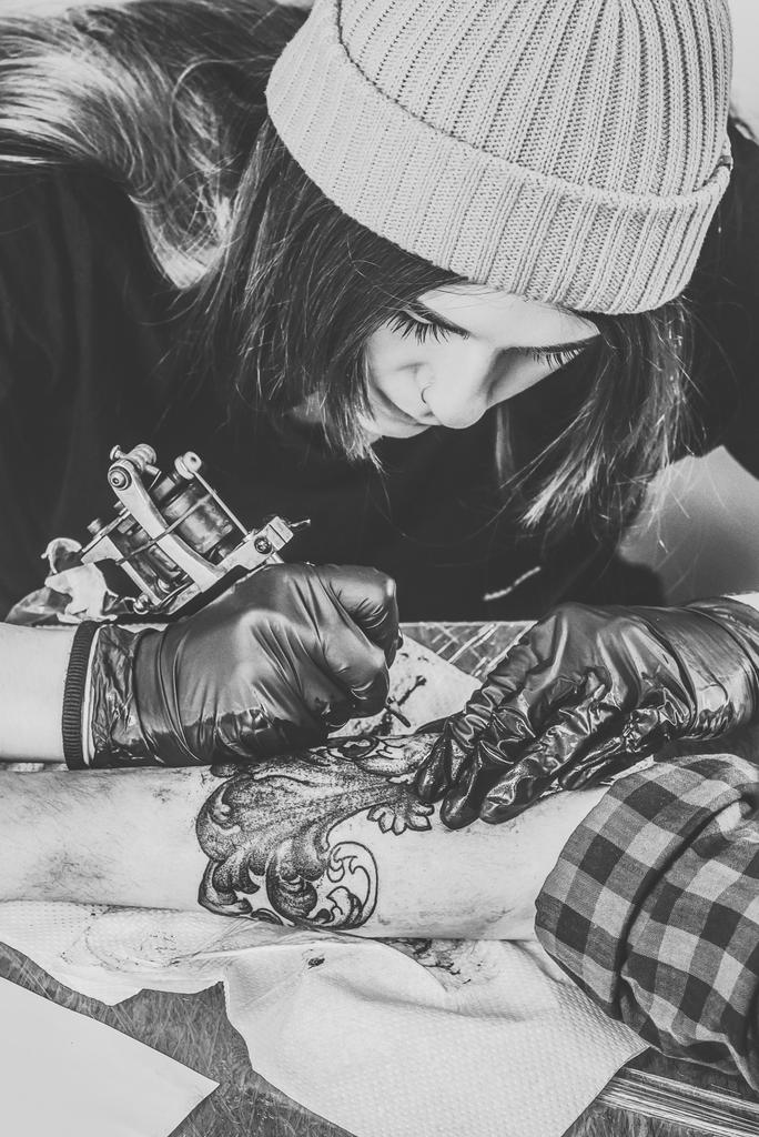 Foto en blanco y negro de la mujer artista del tatuaje en guantes trabajando en la pieza del brazo
 - Foto, imagen