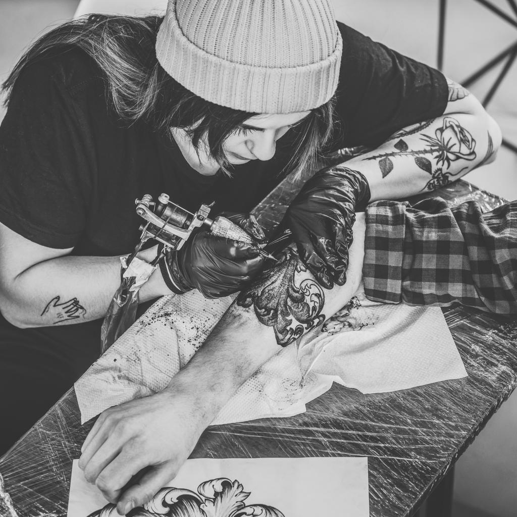 Zwart-wit foto van vrouw tattoo meester en man tijdens het tatoeëren proces in studio - Foto, afbeelding