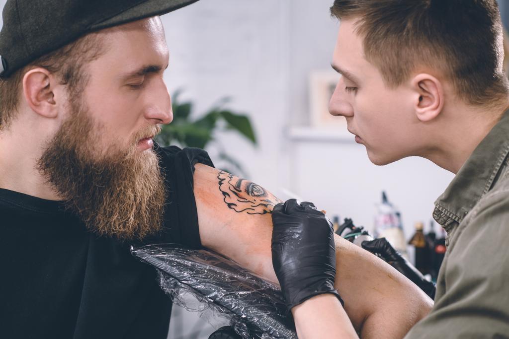 Brodaty mężczyzna i tatuaż opanować w trakcie tattoo Studio - Zdjęcie, obraz