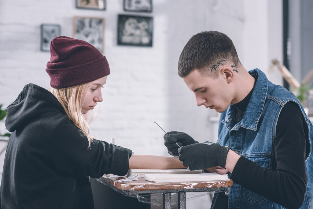 Maestro del tatuaje en guantes trabajando en pieza de brazo en estudio
 - Foto, imagen