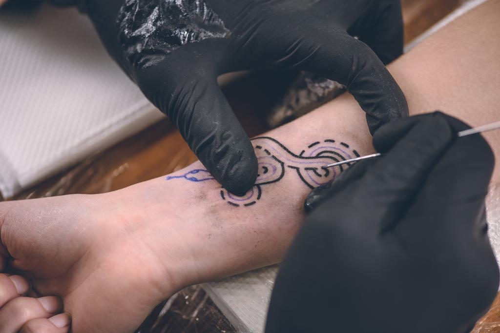 Vue rapprochée du maître de tatouage dans les gants travaillant sur la pièce de bras
 - Photo, image