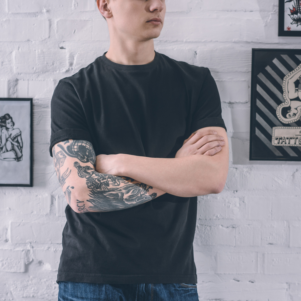 Man with tattooed arm standing by the wall in tattoo studio - Photo, Image