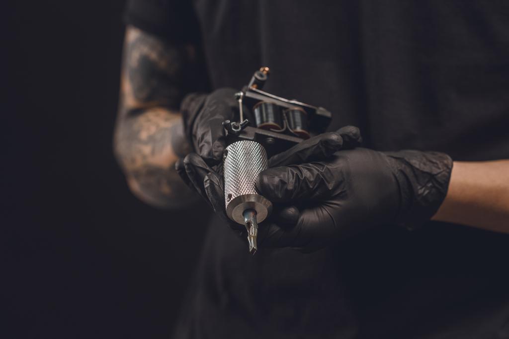 Mannelijke handen in handschoenen houden tattoo machine geïsoleerd op zwart - Foto, afbeelding